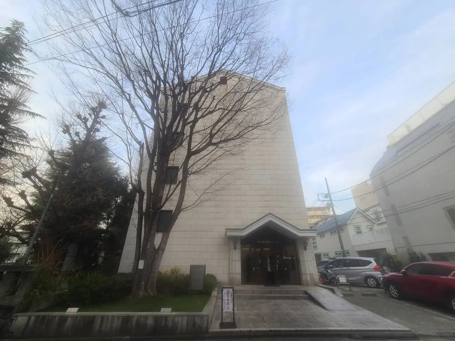 都市の中のモダンな建物のエントランス、周囲に植えられた緑の樹木と駐車場の車