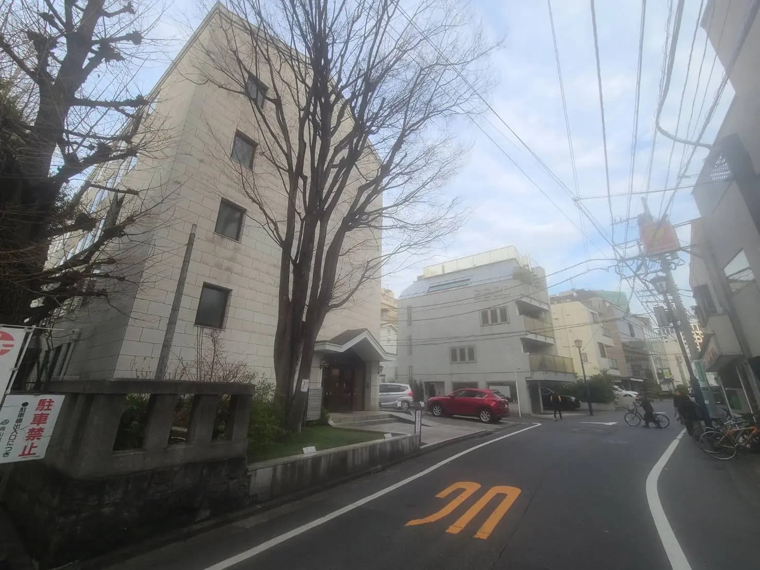 都市の中の交差点、背景にはモダンな建物と青い空、前景には車と自転車が通行する道路