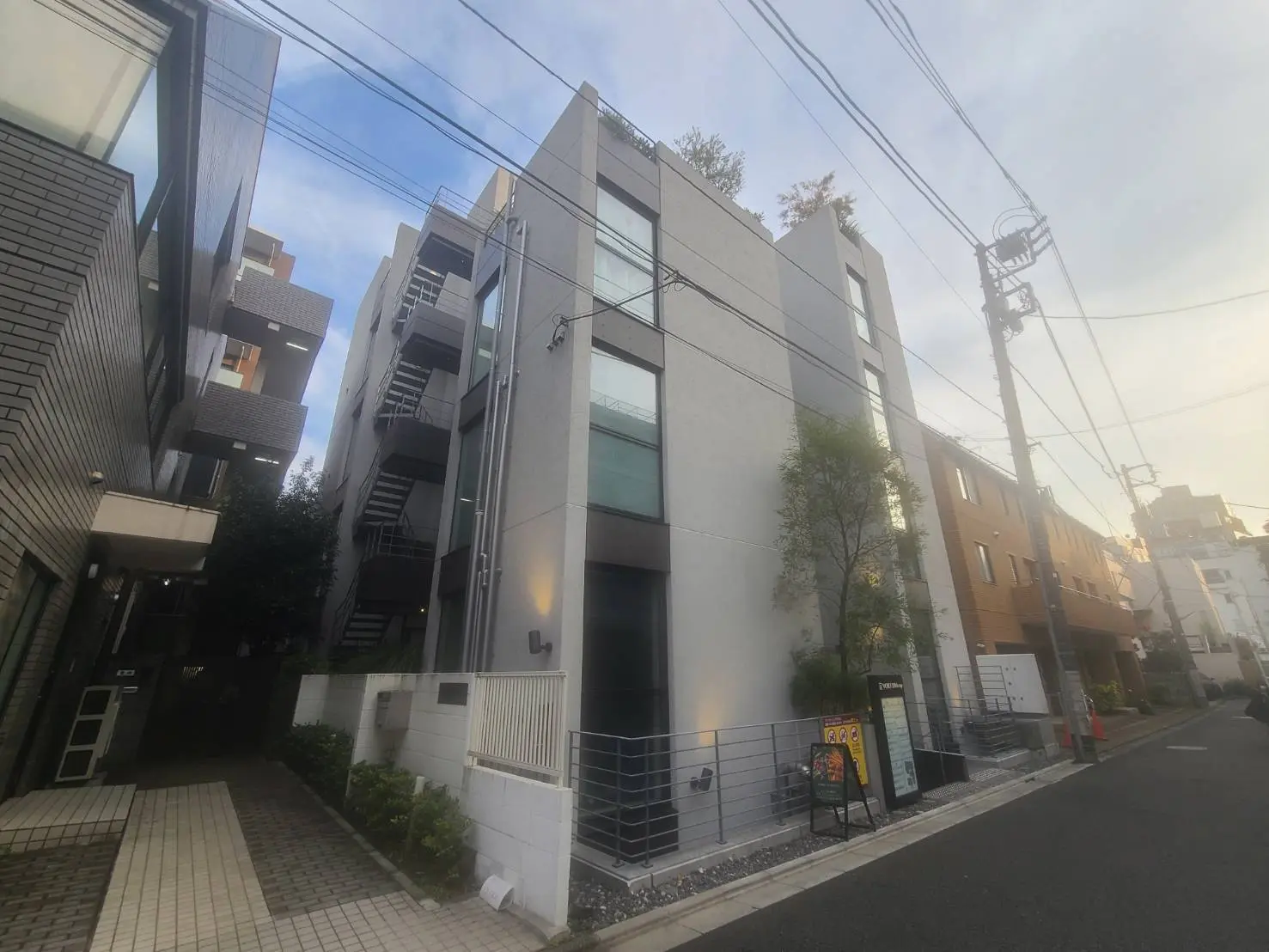モダンな外観の都市型マンション、曇り空の下での住宅街の通り、電線が見える景観