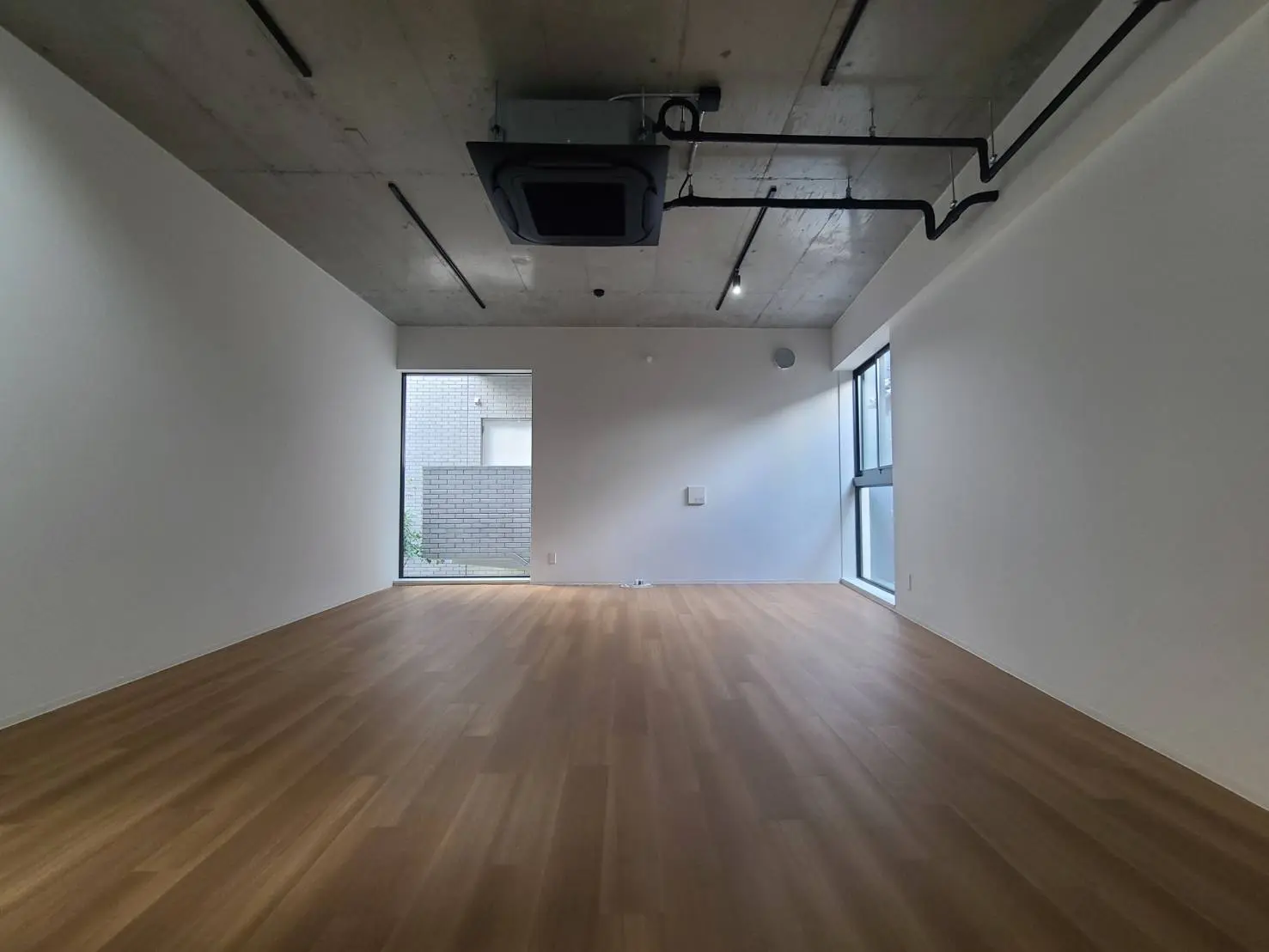 新築マンションの空き部屋、シンプルなデザイン、木製フロア、大きな窓と天井の照明