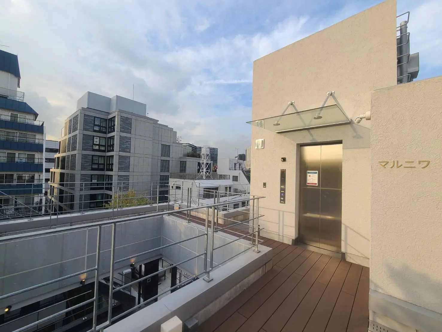 都心のビル群と青空、屋上テラスのウッドデッキ、エレベーター出入り口の外観