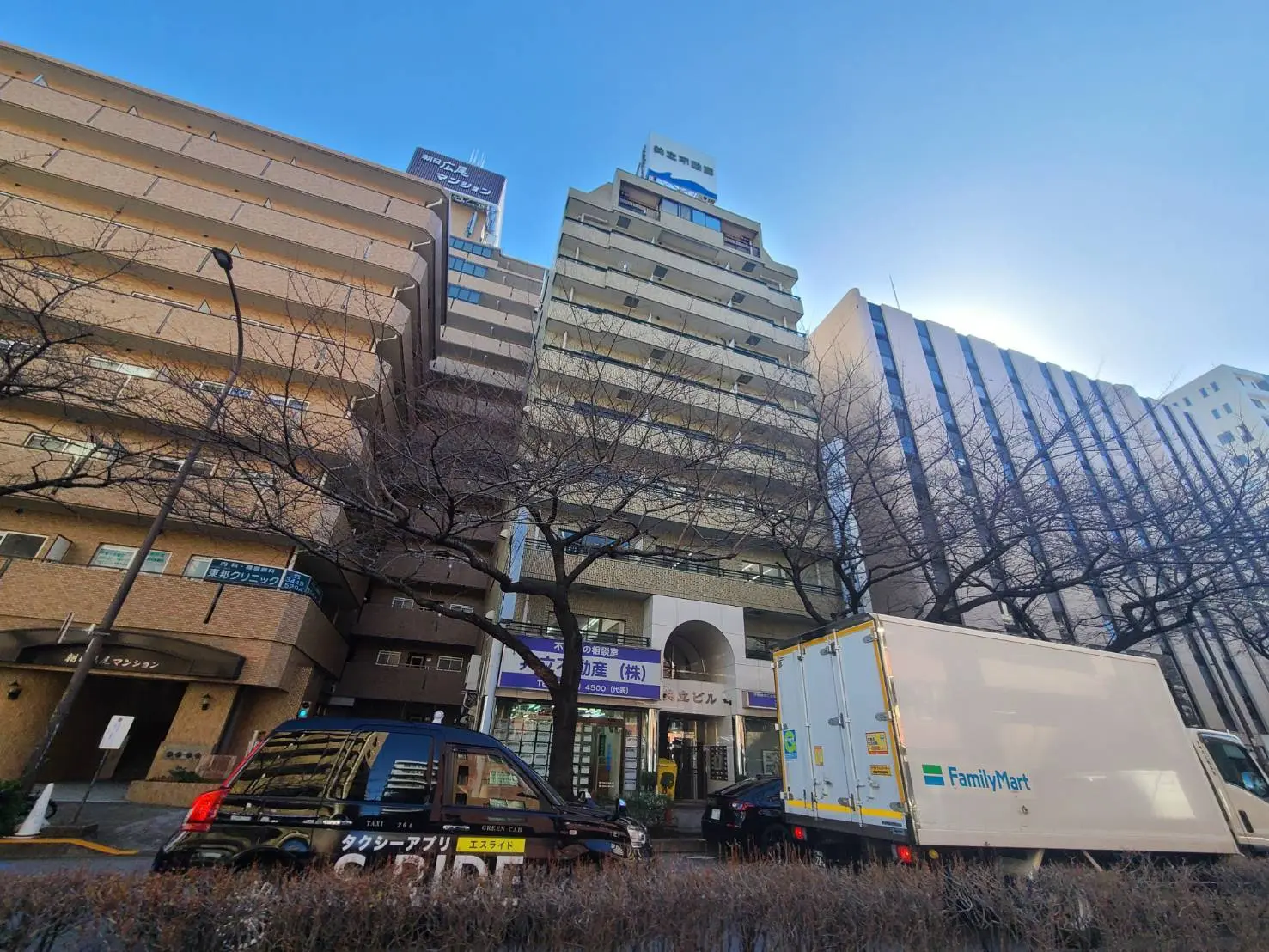 都会の風景、ビルやタクシー、ファミリーマートのトラックが写る市街地の写真