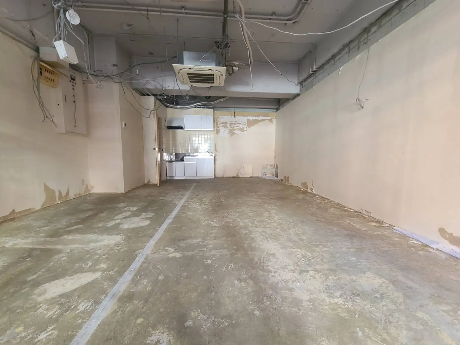 改装前の空き店舗、コンクリートの床と白い壁、天井にはエアコンと電気配線が見える
