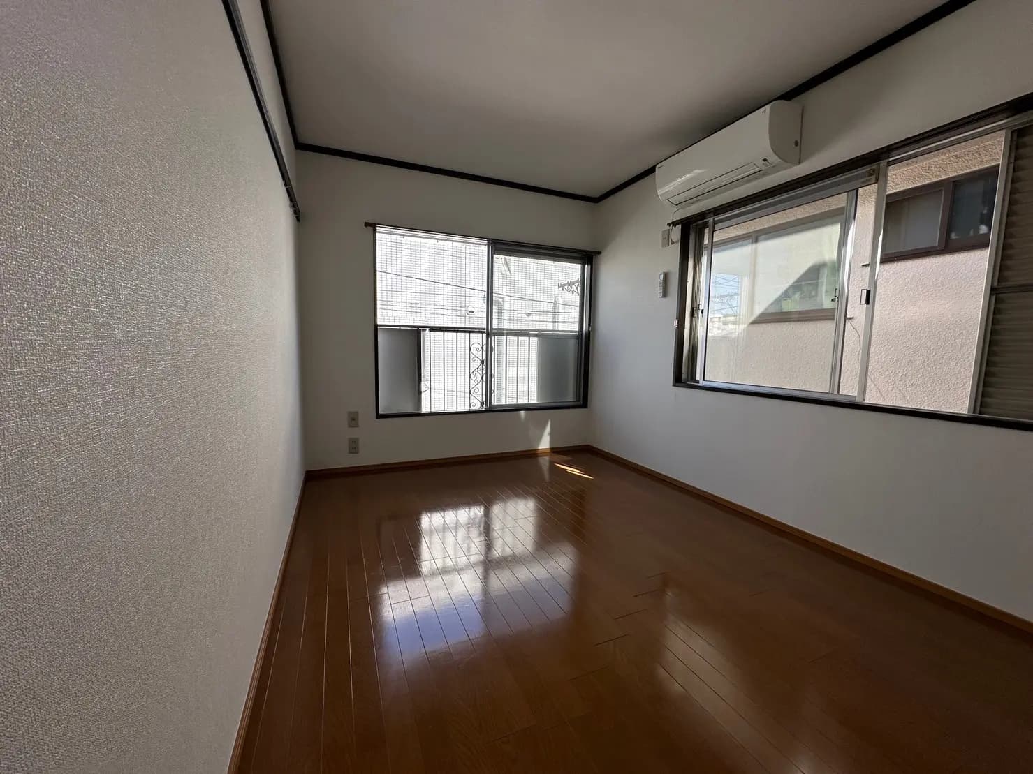 明るく広々とした空き部屋、光沢のある木製フロア、壁には白い塗装、大きな窓とエアコンが付いたインテリア