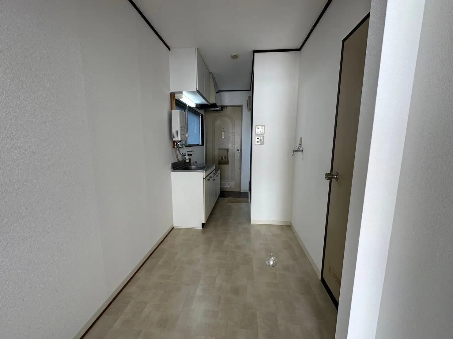 シンプルなデザインのキッチンと玄関、白い壁と茶色の床、クリアな照明のコンパクトな部屋