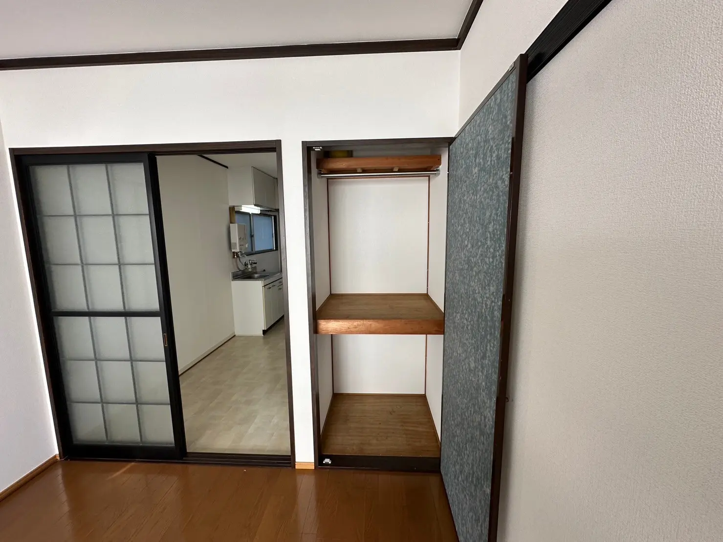 木製のフローリングと収納棚がついた日本風の和室、引き戸のある開放的なキッチンが見えるリビングルーム
