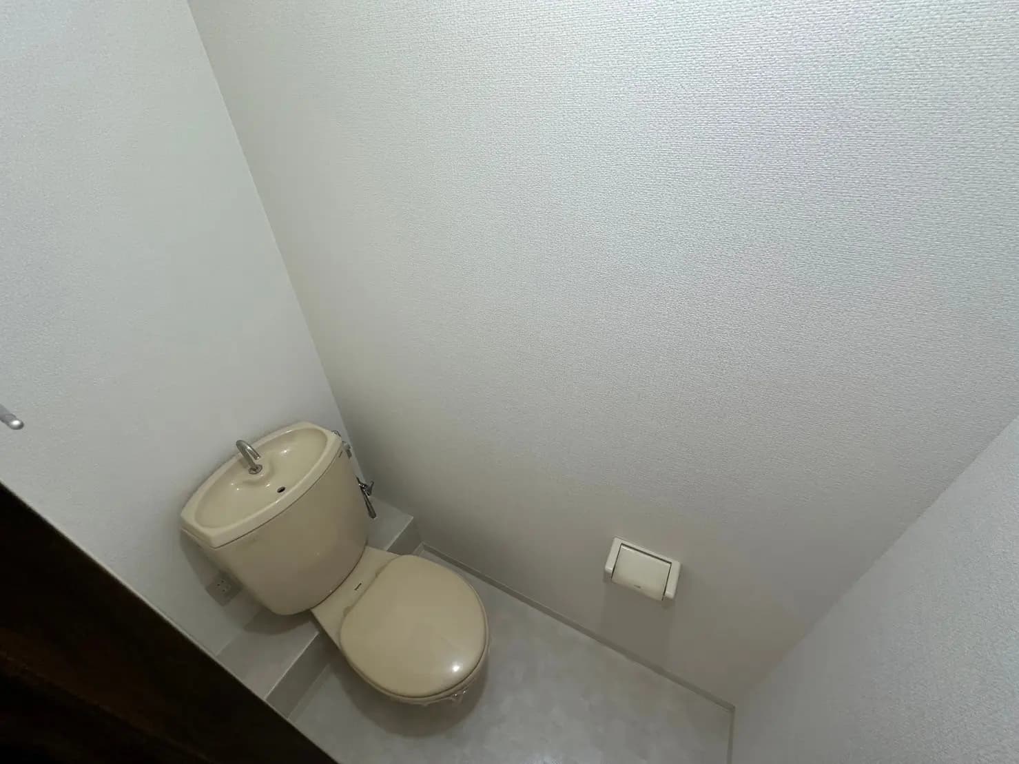 シンプルなデザインのトイレ、白い壁と床、ベージュの陶器製トイレと洗面器