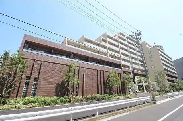 - 現代的なデザインの集合住宅、ブラウンのレンガタイル外壁、緑の植栽と近代的な建物の街並み