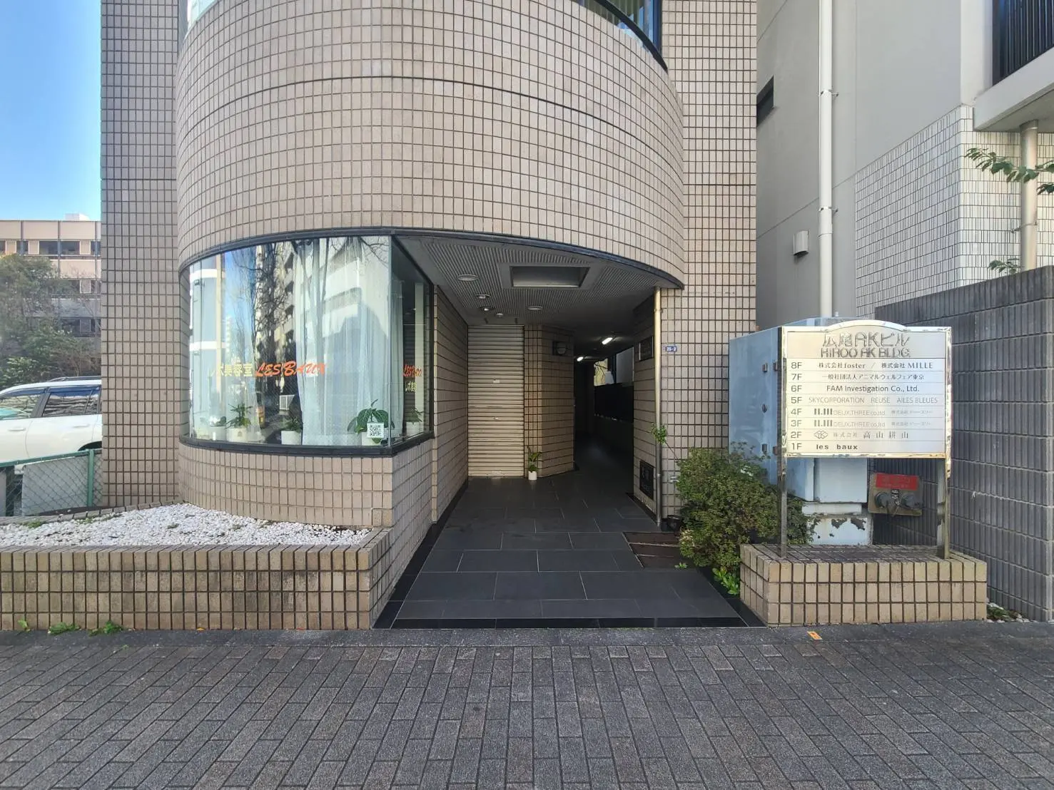 日本のオフィスビルの外観、タイル張りの壁、ガラスのショーウィンドウ、会社看板が見えるエントランス