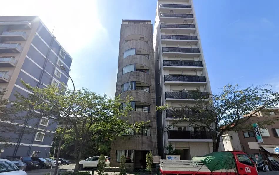 都会の住宅街に立つモダンなマンション、緑の木々と青空が映える外観