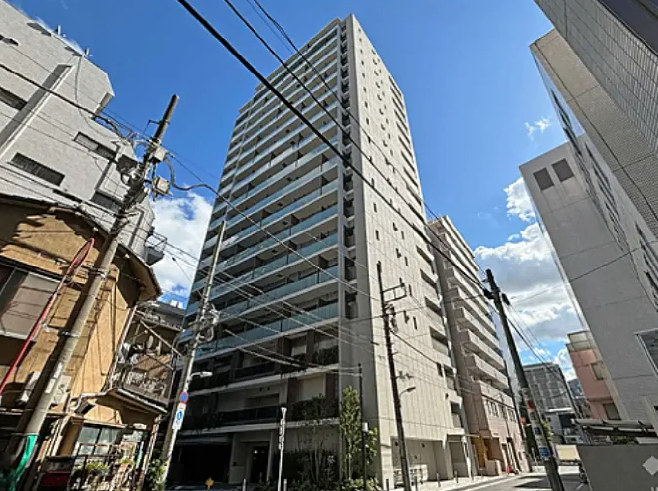 - 近代的な高層マンションと周辺の街並み、晴れた青空と電線が見える都市景観