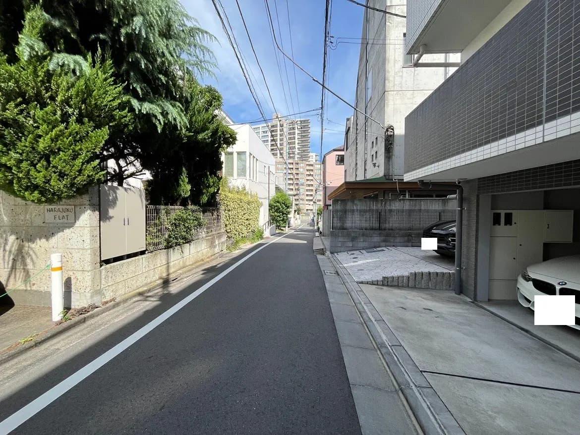 - 原宿エリアの静かな住宅街の風景、緑豊かな木々とシャープなコンクリートビルが並ぶ道路の景観