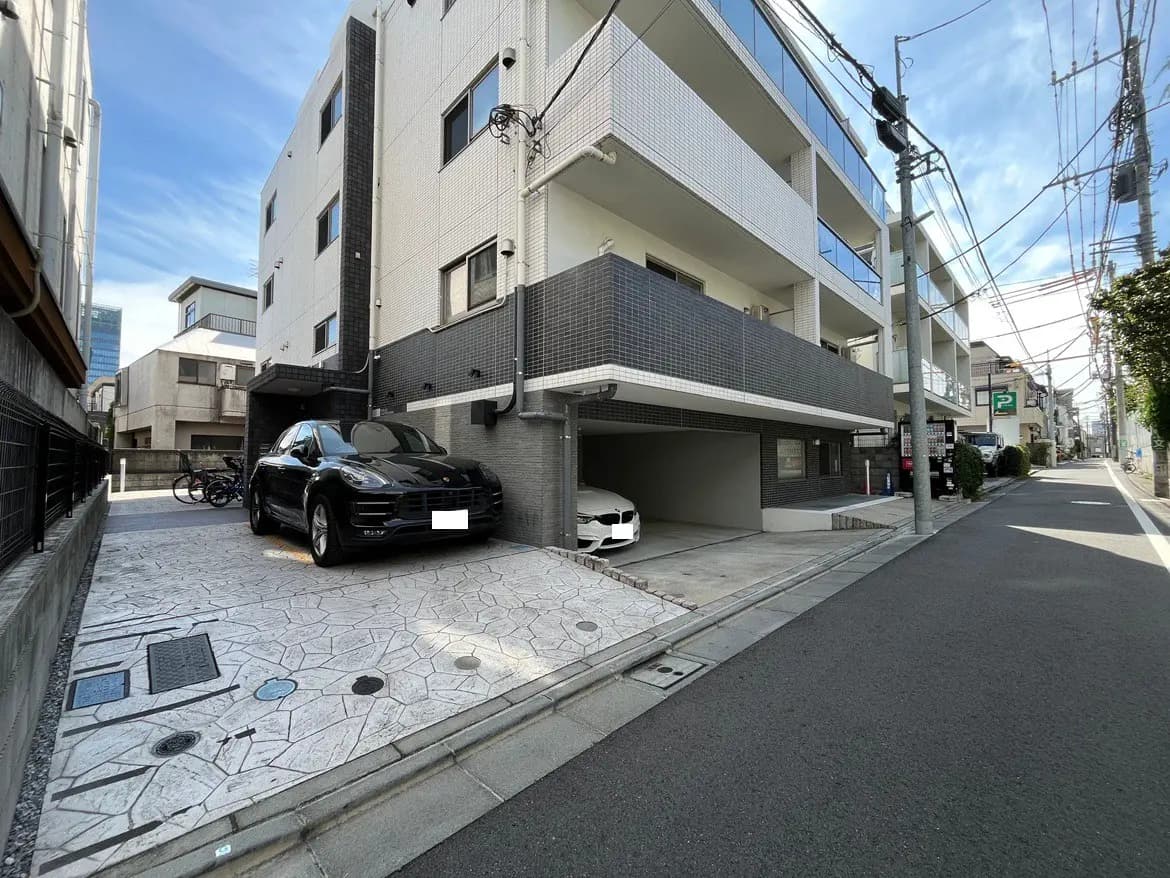 - モダンなアパートメントの駐車場、豪華な黒いSUVと白い車、周囲に自転車と明るい空の風景
