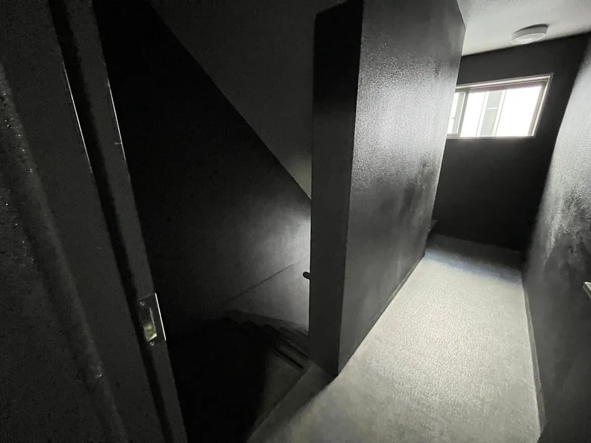 - 黒を基調としたシンプルな階段の内部、薄暗い照明と直線的な壁の構造が特徴の空間