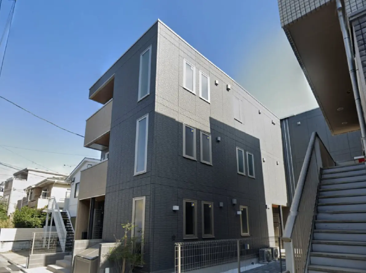 - モダンな外観の三階建てアパート、グレーのタイル張り、窓が多く明るい印象、階段が見えるエントランスの風景