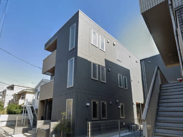 - モダンな外観の三階建てアパート、グレーのタイル張り、窓が多く明るい印象、階段が見えるエントランスの風景