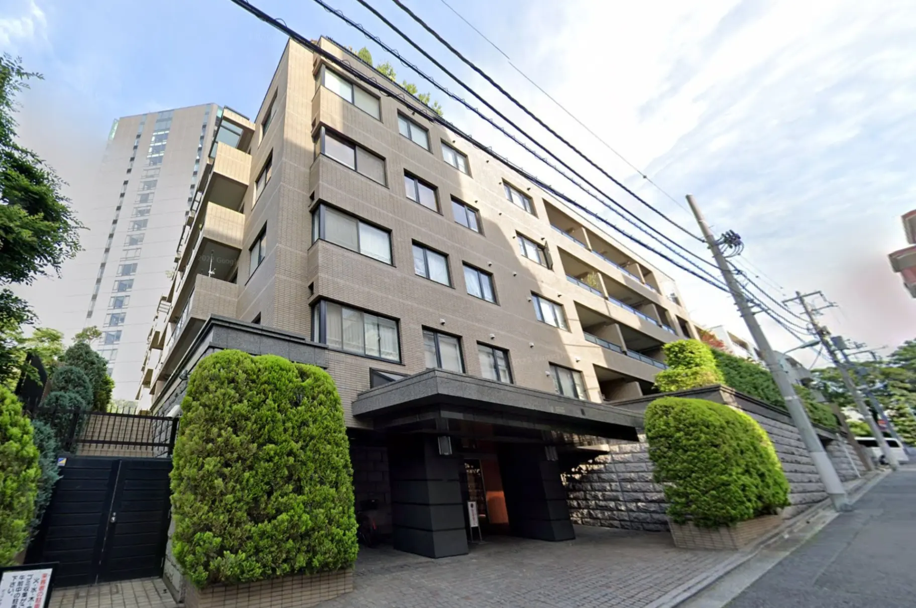 都心に位置するモダンなマンションの外観、緑の植栽とエントランス、電線が見える街並み