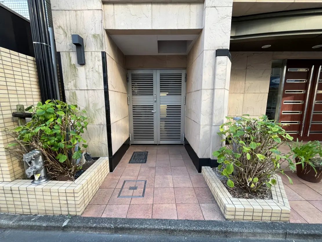 - 植木が飾られたエントランスの外観、格子戸と石造りの壁がある建物の入り口