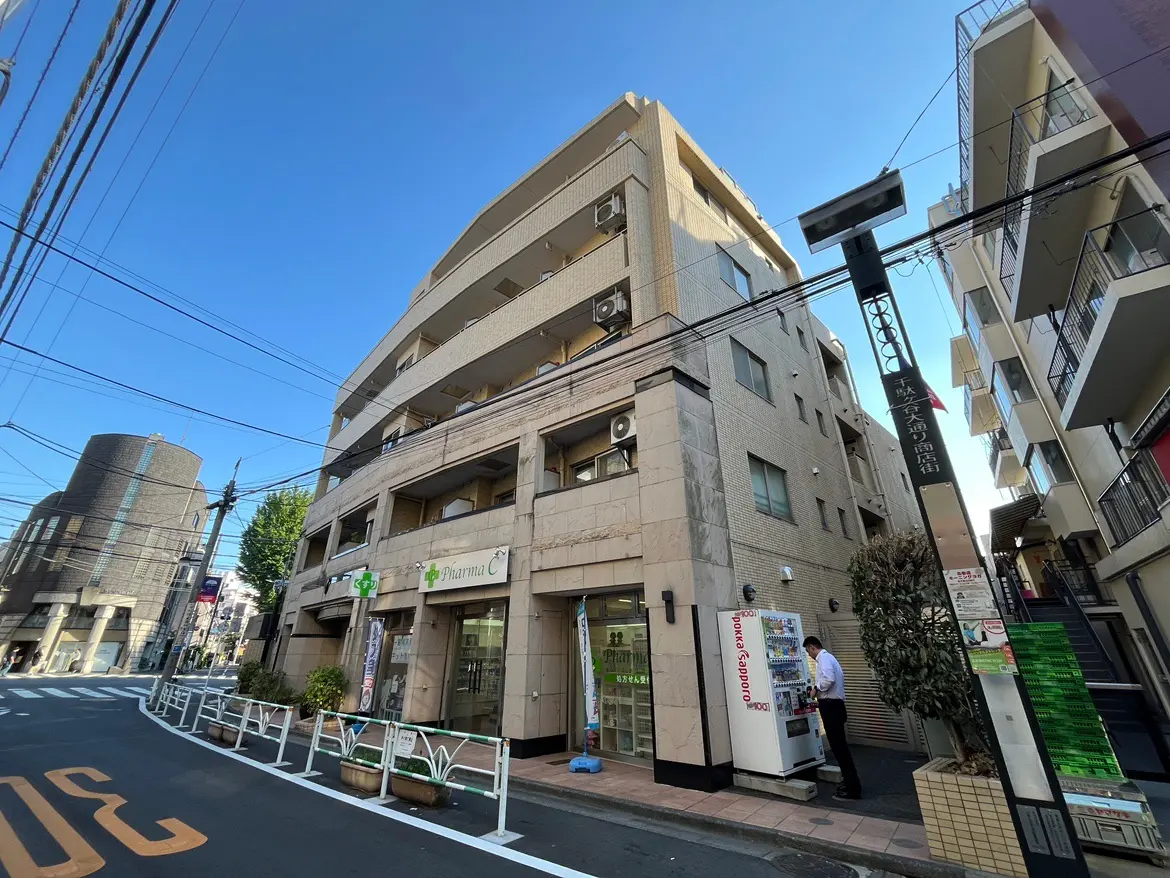 - 商業施設が並ぶ街角の風景、薬局の看板が目立ち、青空の下に建物が並ぶ都市の一角