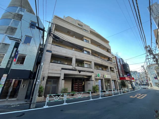 - 都市の中心部にある四階建てのマンション、周囲に商業施設が立ち並び、電柱と電線が視界に入る風景