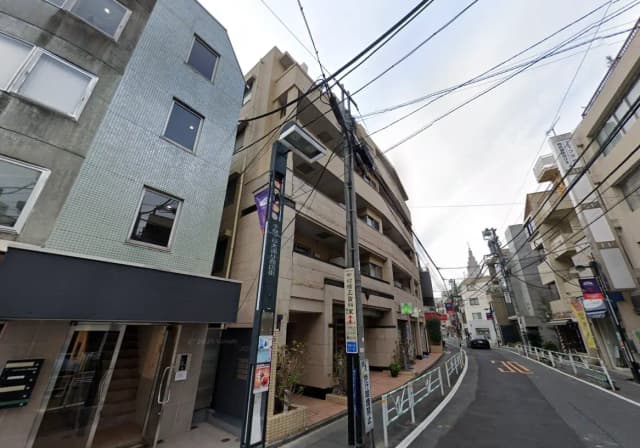 - 複数のビルが立ち並ぶ都会の街並み、左側はタイル張りの外壁、右側はコンクリート造の建物、電線が交差する様子が見える道路の風景
