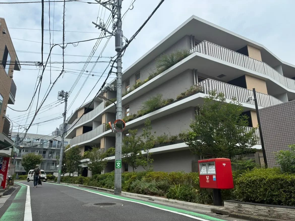- 都市の風景に佇む現代的なアパートメントビル、緑豊かなバルコニーと郵便ポストがある通りの景観