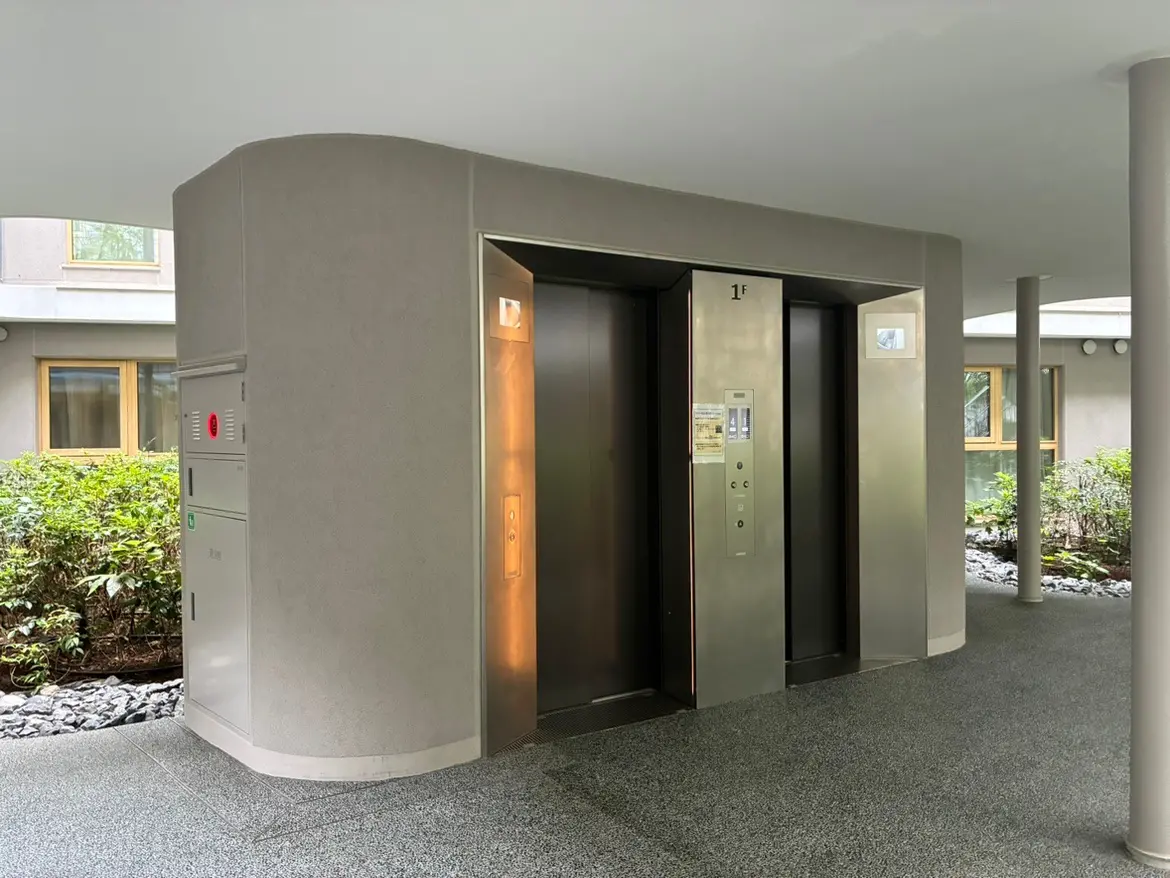 - モダンなエレベーターが設置された建物のエントランス、周囲に緑の植物が植えられたデザインの様子