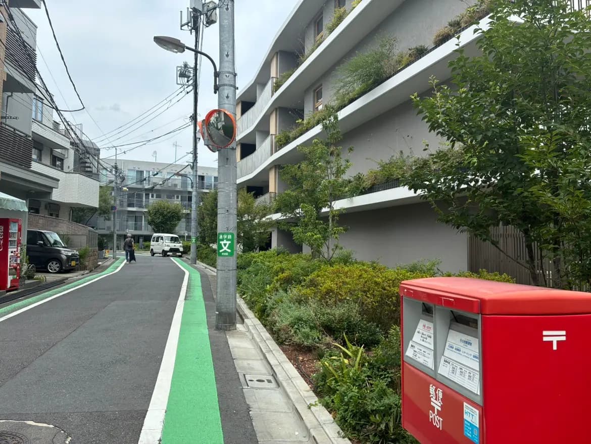 - 緑の自転車レーンが描かれた都市の道路と、隣接する郵便ポスト、近隣の建物と植栽が見える風景