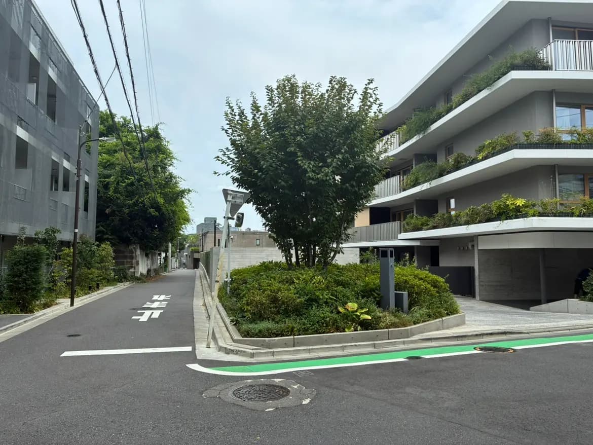 - 都市の住宅街にあるモダンなアパートメントビルと緑豊かな植物、広い歩道が特徴的な風景