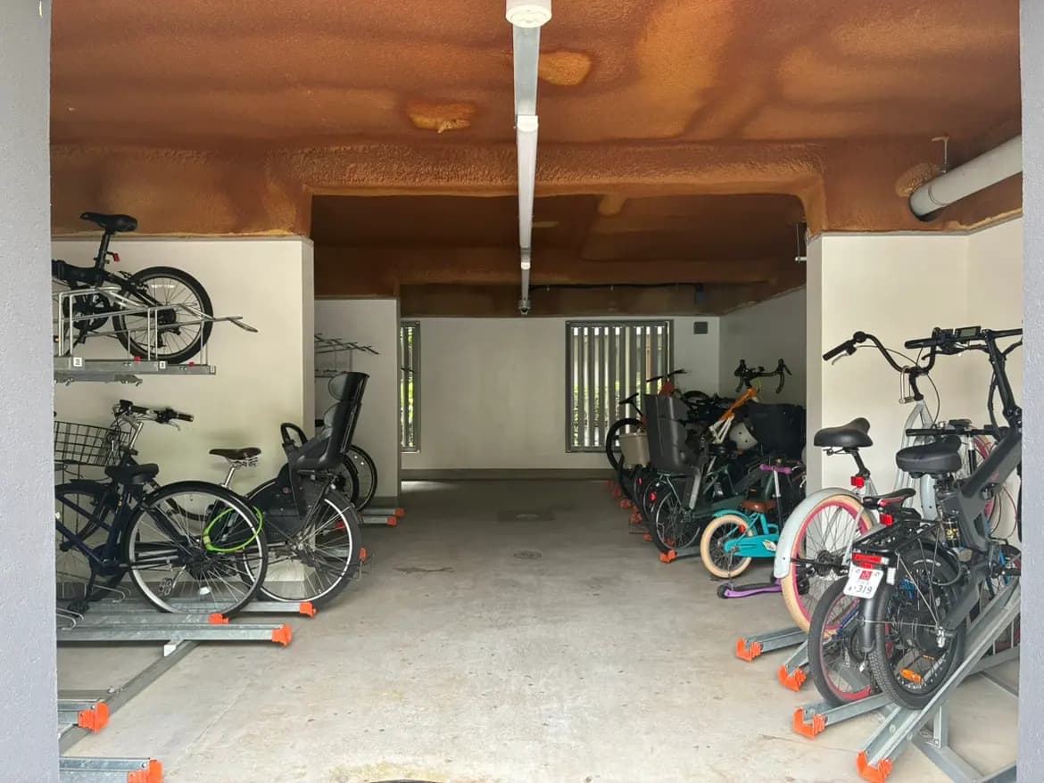 - 自転車が整然と収納された駐輪場、壁に並ぶラックと明るい照明のオープンスペース
