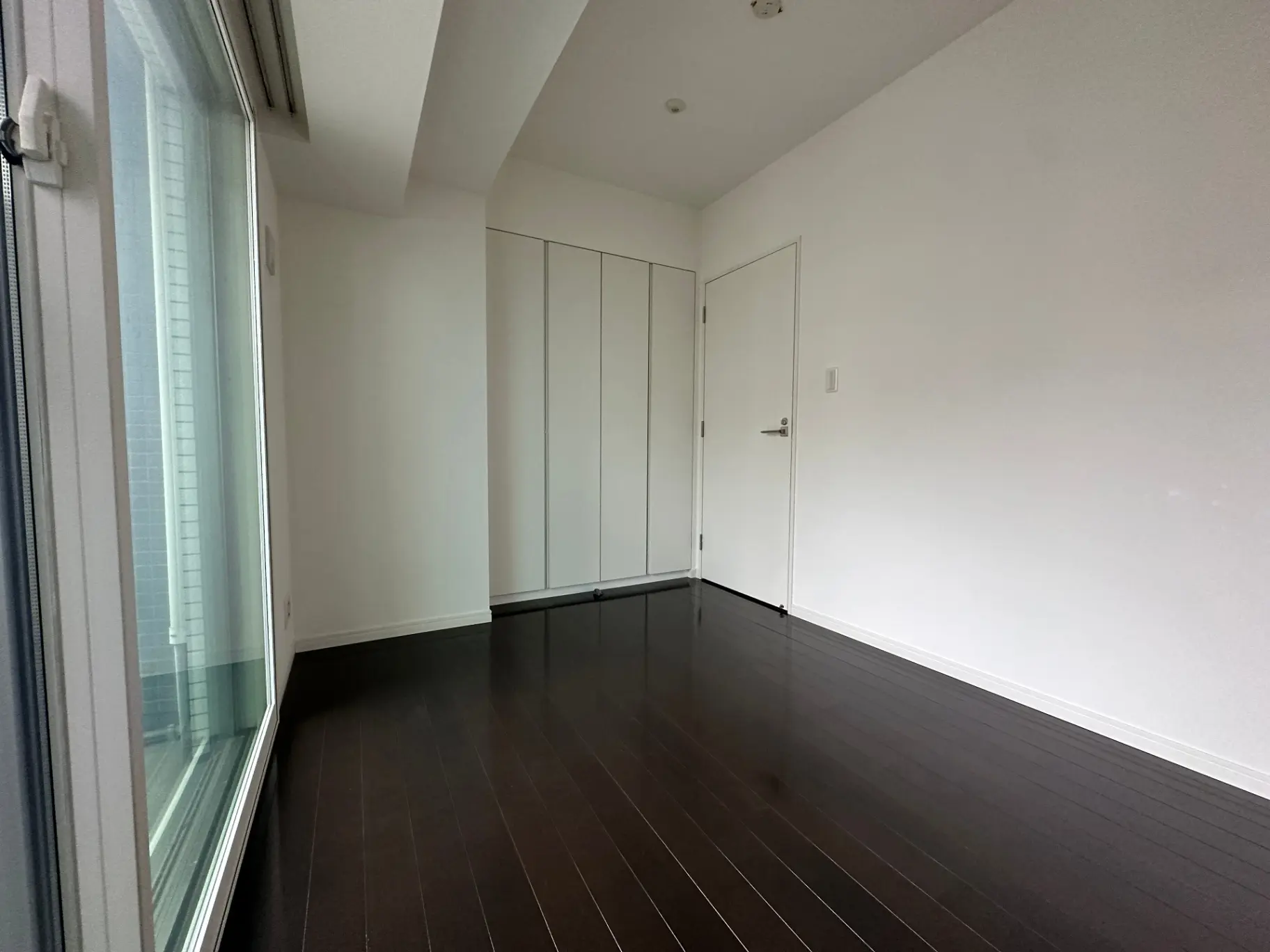 明るく広々とした白い壁と茶色のフローリングの空き部屋、左側には大きな窓とカーテンが設置