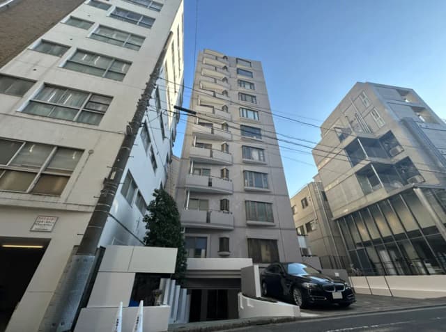 都市部の現代的なマンションの外観、駐車場には黒い高級車、青空とビルの影が美しい景観