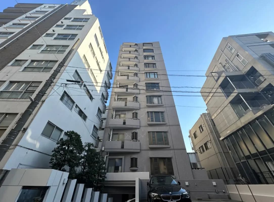 都市の高層マンション、青空と現代的な外観の建物、駐車スペースに停まる高級車