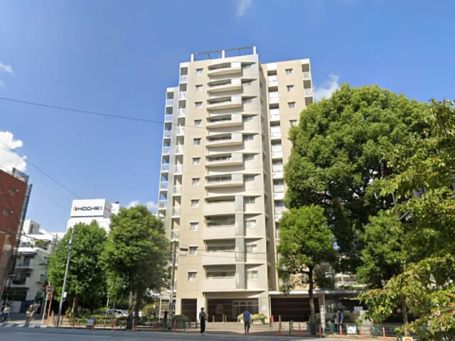 高層マンションの外観、青空に映えるシンプルなデザインと周囲の緑豊かな木々の景観