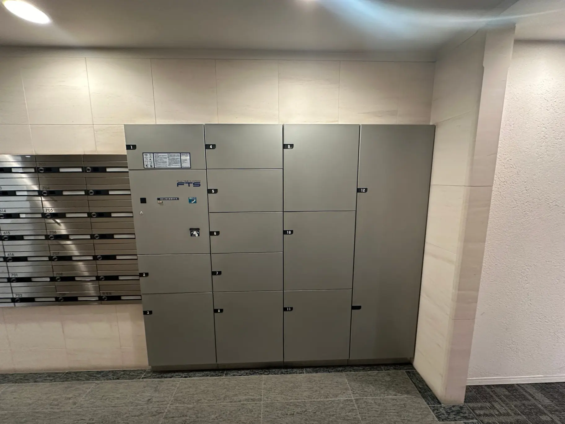マンションのエントランスに設置された宅配ボックスと郵便受け、床はタイル張りで壁はライトグレーのインテリア