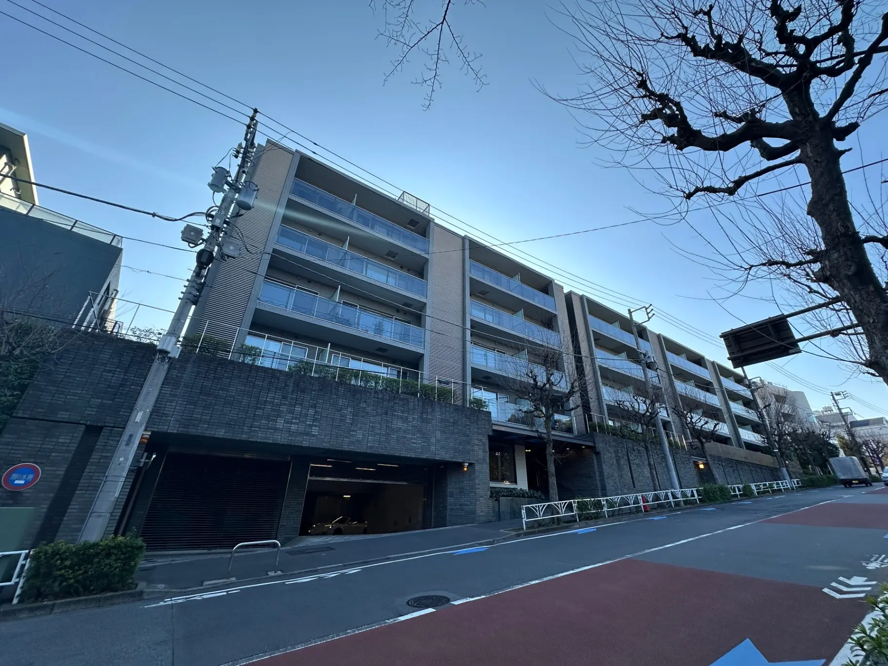 現代的な外観のマンション、駐車場入り口、晴れた日の街路樹、青空