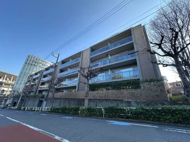 現代的な外観のマンション、青空と木々が映る窓、清潔感のある住宅街