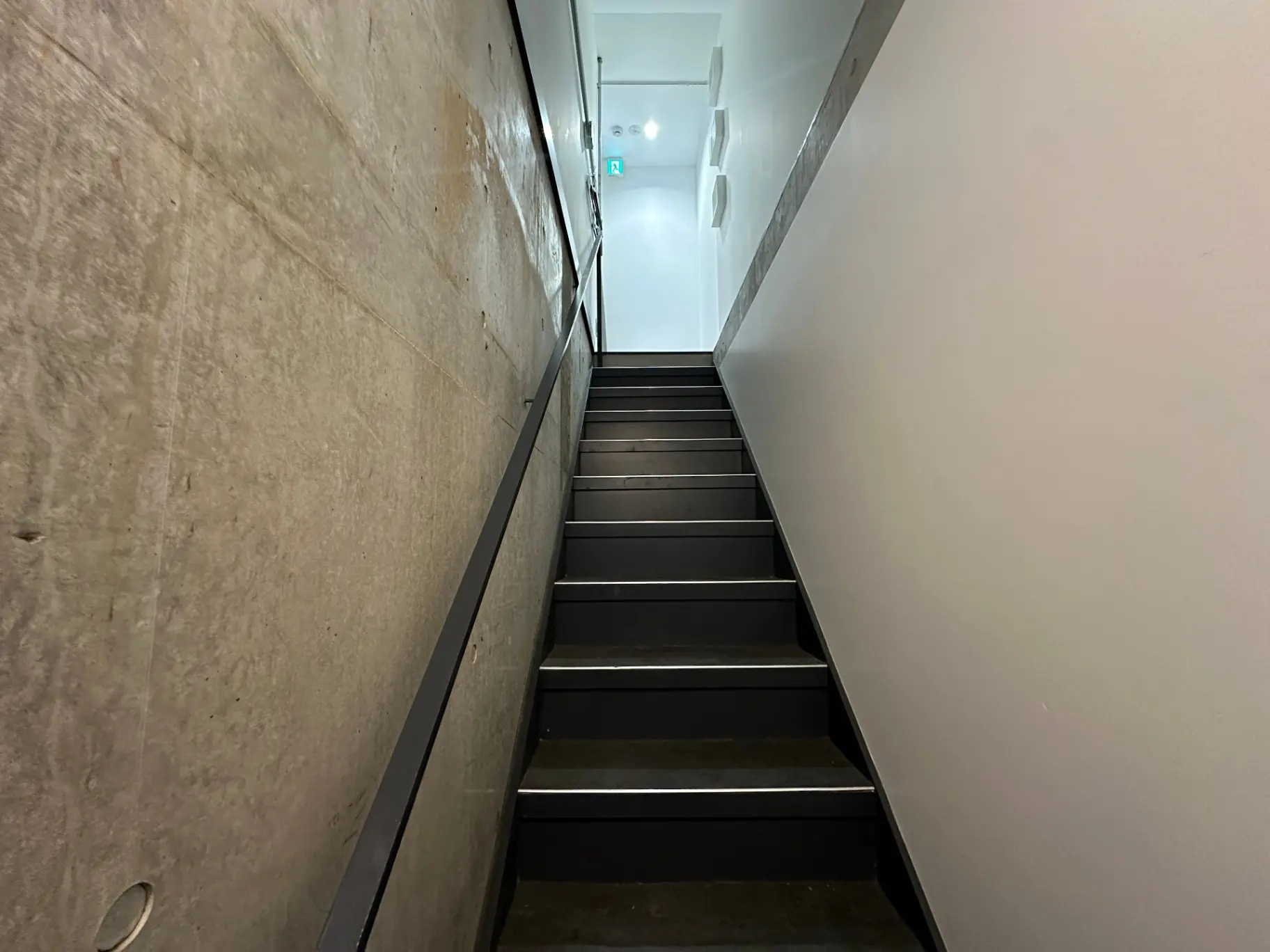 建物内の狭い階段、コンクリートと階段の手すり、上へと続く明るい出口