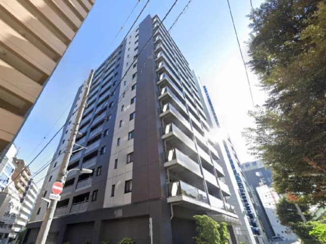 - 高層マンションの外観、近くの道路に立つ電柱と街灯、明るい空と日差しが映える風景