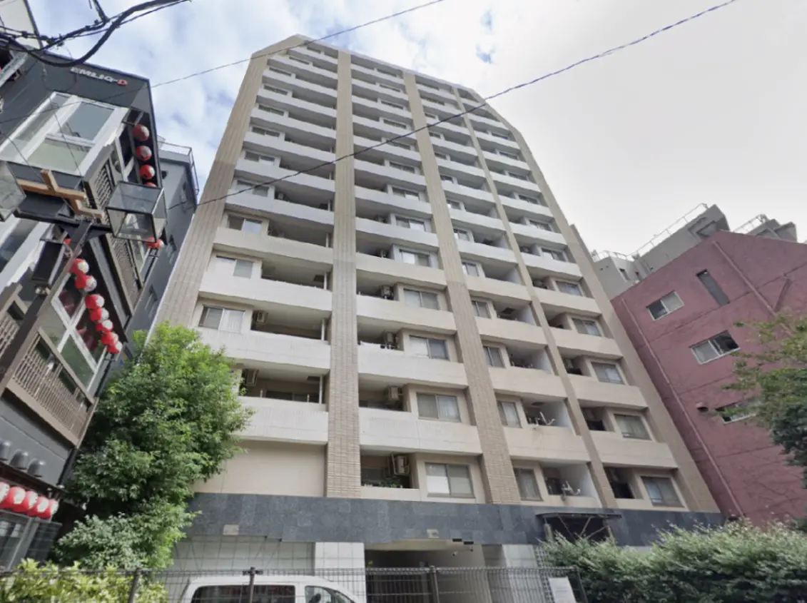 - 都市型のマンション外観、数階建ての構造、隣接する建物と緑豊かな植栽が見える街並み