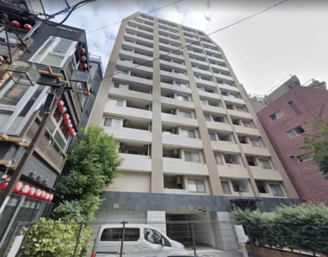- 都市型マンションの外観、近隣のビルと並ぶ現代的なデザイン、周囲には緑が見える景観