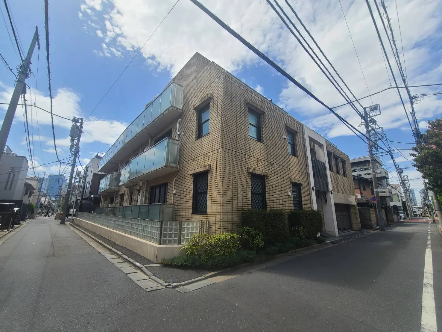 都会の住宅街にあるモダンなデザインのアパート、明るい日差しと青空が映える外観