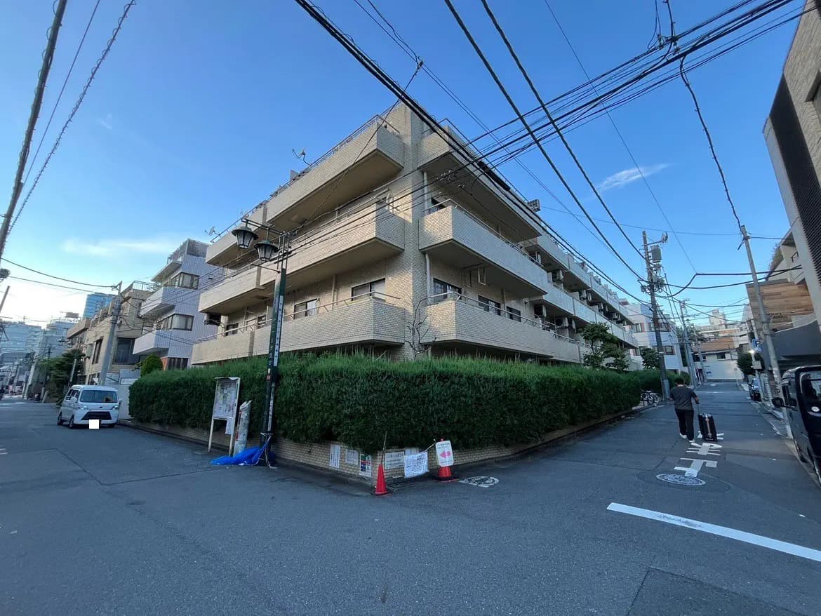 - 住宅街の角に位置するコンクリート造りのマンション、青空と電線が見える風景