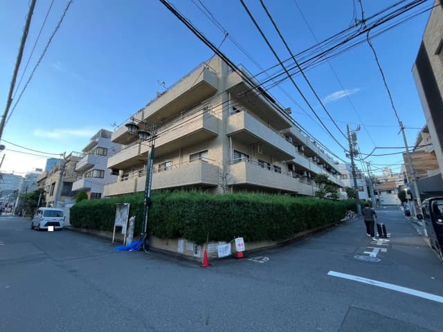 - 住宅街の角に位置するコンクリート造りのマンション、青空と電線が見える風景