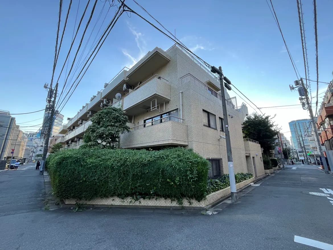 - 住宅街の角に立つレンガ造りのアパートメント、周囲には緑豊かな植栽と電柱が並ぶ景色