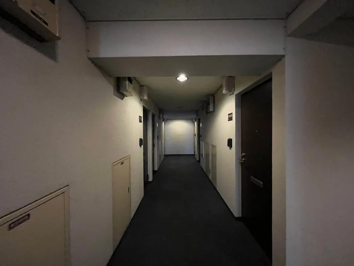 - 照明が落ち着いた雰囲気を醸し出す長い廊下、壁に取り付けられた空調設備と扉が並ぶ、シンプルなデザインのインテリア