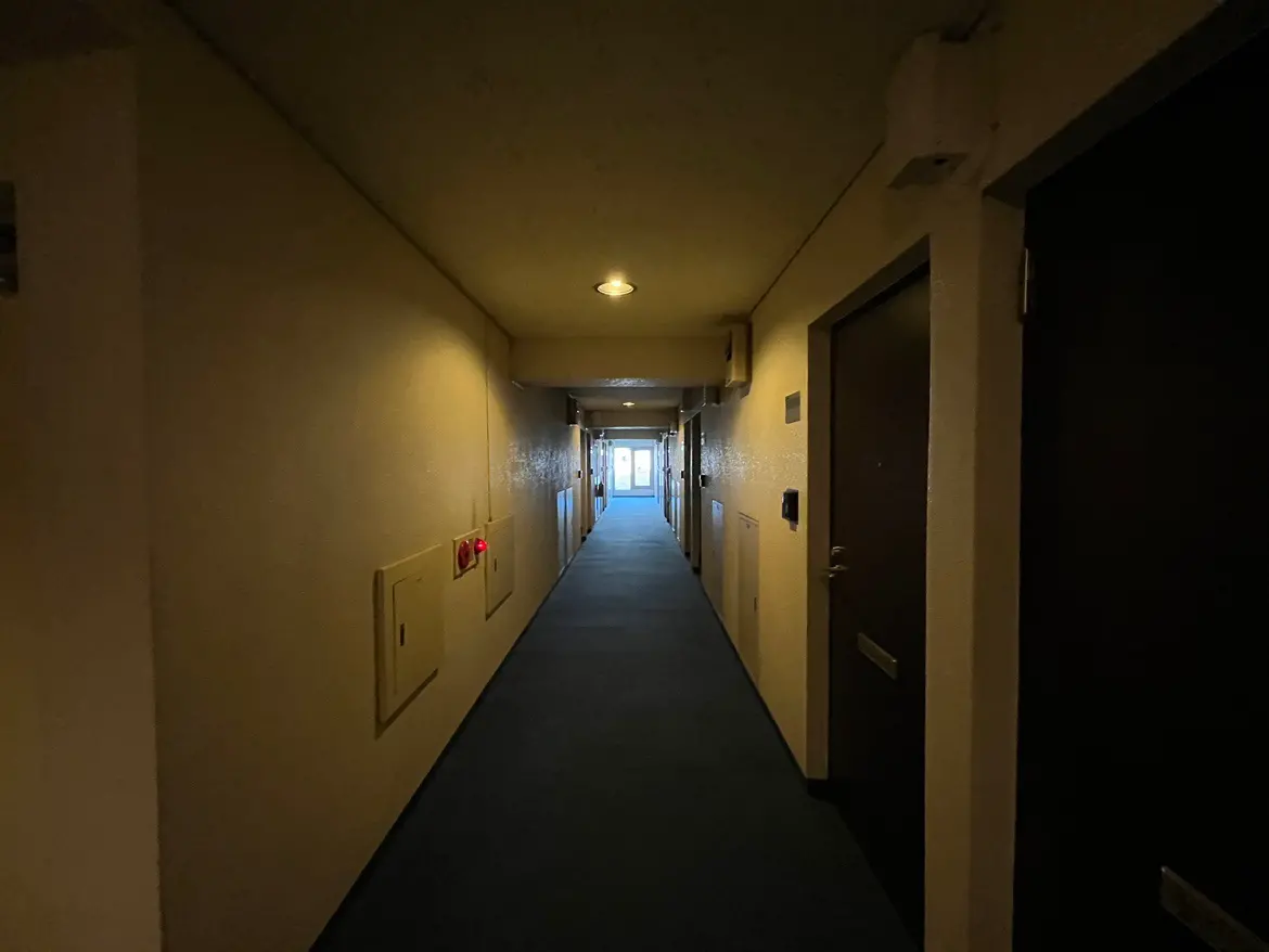 - 照明のある静かな廊下、両側にドアが並び、遠くの自然光が差し込む明るい空間