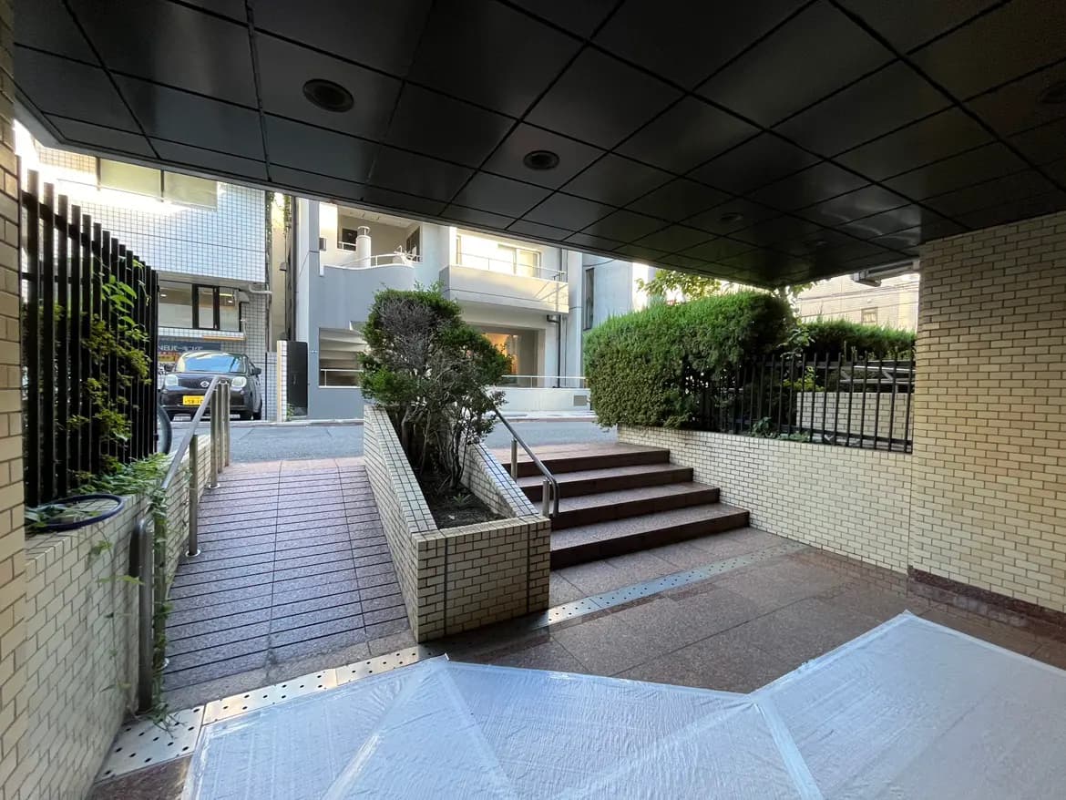 - 屋外のアプローチ、石畳のスロープと階段、緑の植栽が配されたモダンなエントランスの風景