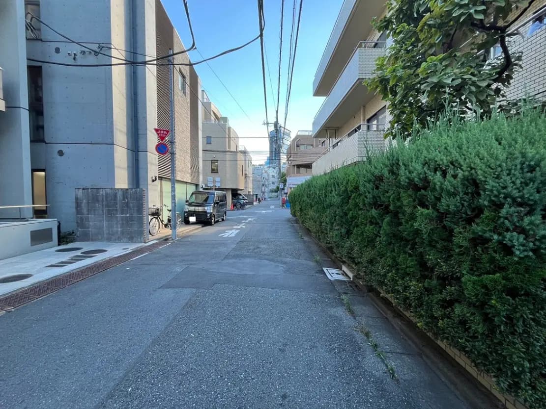 - 都市の住宅街の静かな通り、両側にコンクリート製の建物と緑豊かな生垣がある風景