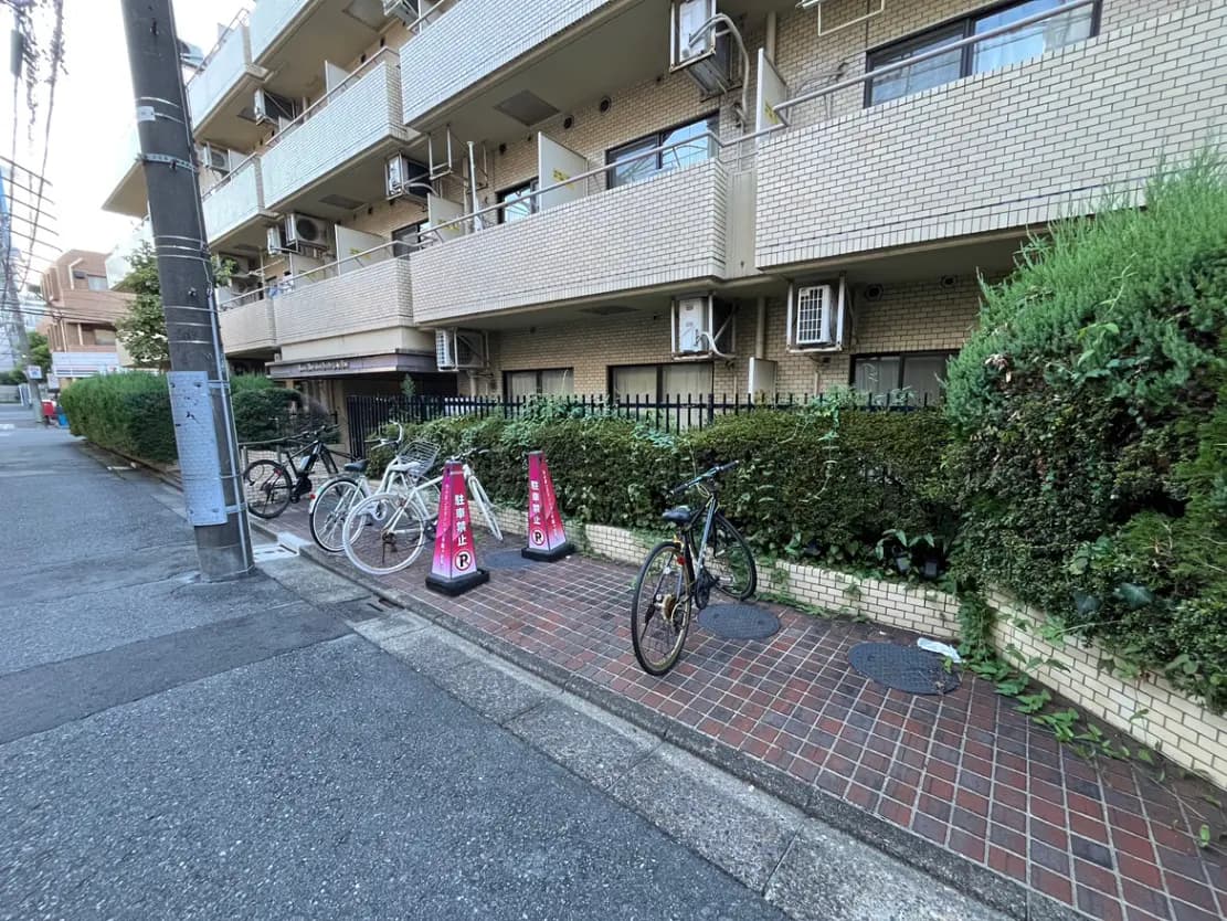 - 自転車が停められた公団の外観、緑の生け垣と舗装された歩道のある静かな街並み